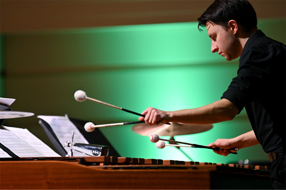 Male student, wearing smart attire, playing the marimba with mallets, in a chamber performance to an audience.